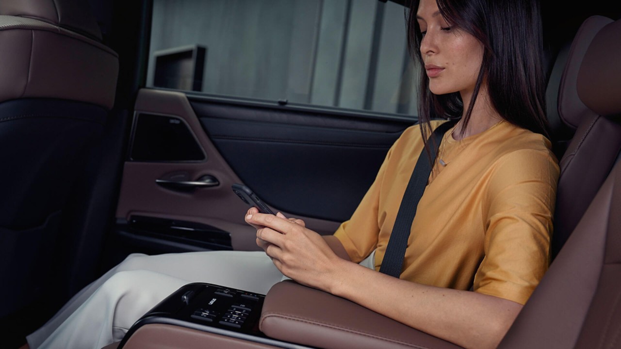 Een vrouw met haar telefoon zat op de achterbank van een Lexus ES.