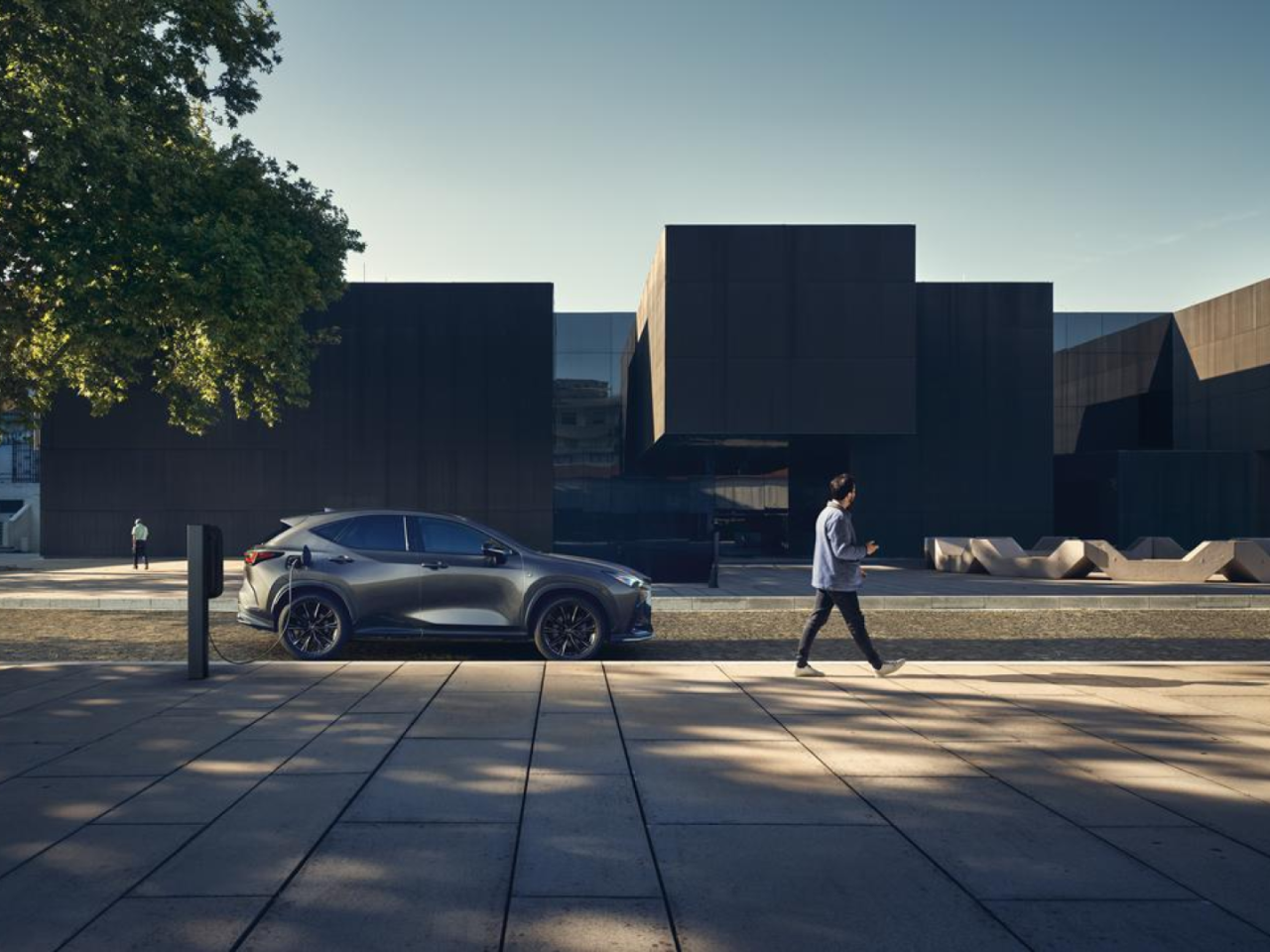 Een persoon loopt langs een ingeplugde Lexus NX
